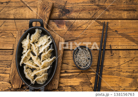 Boiled Asian dumplings potstickers sprinkled with sesame in black skillet on natural wood table authentic oriental cuisine. 138156763