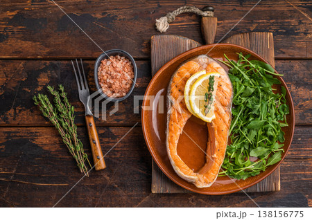 A wholesome grilled salmon portion paired with zesty citrus and vibrant greens arranged on a brown plate against rich wooden tones for hearty food imagery. A wholesome grilled salmon portion paired with zesty citrus and vibrant greens arranged on a brown plate against rich wooden tones for hearty food imagery. 138156775