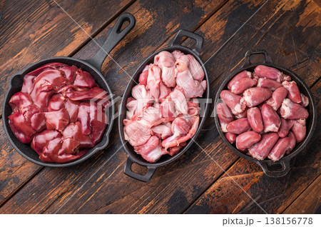 Raw chicken liver, gizzards, and hearts in cast iron pans on rustic wooden background, fresh poultry offal cooking ingredients. 138156778