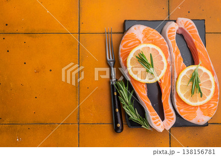 Fresh raw sea trout steaks with lemon and rosemary arranged on a dark slate board over a warm terracotta tile background perfect for premium food visuals. Fresh raw sea trout steaks with lemon and rosemary arranged on a dark slate board over a warm terracotta tile background perfect for premium food visuals. 138156781