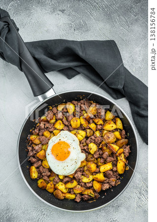Skillet breakfast hash of crispy potatoes and minced beef topped with sunny egg on textured gray background for culinary and recipe use. 138156784