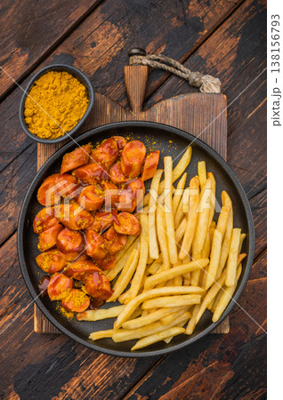 German currywurst with fries on a black plate over rustic wooden background perfect for street food visuals and fast food stock images. 138156793