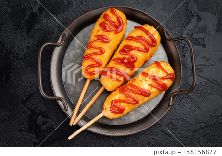 Golden corn dogs with ketchup topping served on plate with sauce, crunchy fast food snack on dark background 138156827