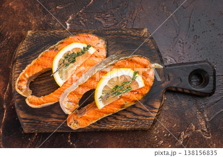 Closeup grilled salmon steaks chum with juicy texture and char marks, thyme and lemon on dark background Closeup grilled salmon steaks chum with juicy texture and char marks, thyme and lemon on dark background 138156835