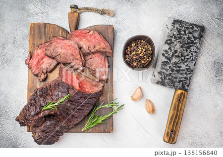 Cooked hanger steak diaphragm beef cut sliced with juicy medium doneness, herbs garlic and spices on board, clean light background 138156840