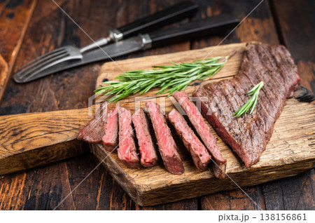 Cooked beef steak sliced into pieces on wooden board with cutlery, medium rare meat with texture and fibers, preparation concept 138156861