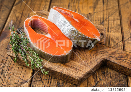 Closeup raw salmon steaks sockeye with bright orange flesh, thyme and lemon slices on rustic wooden background Closeup raw salmon steaks sockeye with bright orange flesh, thyme and lemon slices on rustic wooden background 138156924