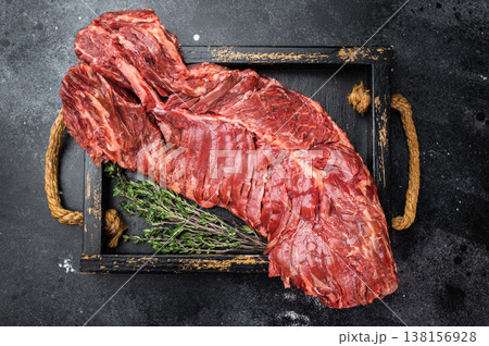 Raw beef hanger or onglet steak on black tray with rope handles over dark stone background, strong contrast and copy space 138156928
