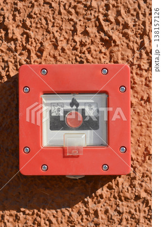 Red fire alarm manual call point on a textured orange wall 138157126