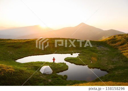 Small alpine lake reflecting sunrise light surrounded by green grass 138158296
