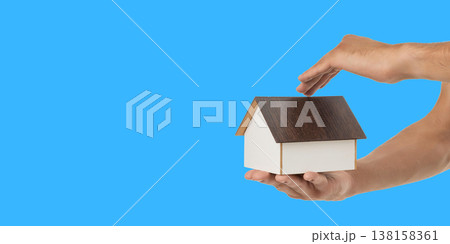 Hands hold a house model with a wooden roof Hands hold a house model with a wooden roof 138158361