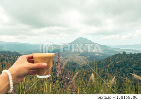 Holding a glass of coffee with mountains in the background Holding a glass of coffee with mountains in the background 138158386