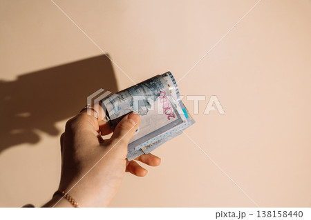 Hand holding a stack of Kazakhstani tenge banknotes on beige background with hard shadow, cash concept Hand holding a stack of Kazakhstani tenge banknotes on beige background with hard shadow, cash concept 138158440