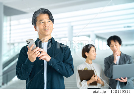 オフィスでスマートフォンを手に未来を見つめる中高年男性と協力するビジネスチーム 138159515