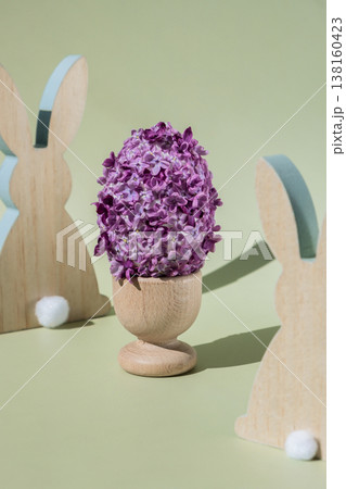 Wooden minimalism low-key bunny decor. Easter egg made of lilac spring flowers in pastel green background. Sustainable holiday minimalistic still life composition. Copy space template for invitation Wooden minimalism low-key bunny decor. Easter egg made of lilac spring flowers in pastel green background. Sustainable holiday minimalistic still life composition. Copy space template for invitation 138160423