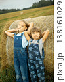 Two cheerful village girls in overalls are standing, leaning on a haystack. 138161029