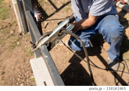 Male welding metal fence outdoors with sparks flying in daylight. National Welding Month 138161963