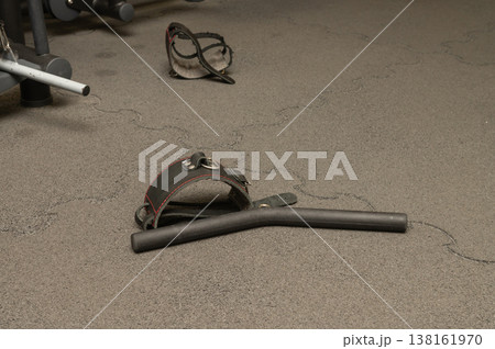 Gym equipment on rubber floor: handlebar, adjustable dumbbell, safety strap Gym equipment on rubber floor: handlebar, adjustable dumbbell, safety strap 138161970
