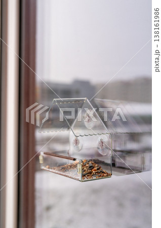Transparent window bird feeder with seeds in a winter urban setting 138161986