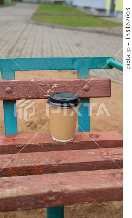 Disposable coffee cup on weathered wooden park bench in urban setting Disposable coffee cup on weathered wooden park bench in urban setting 138162003