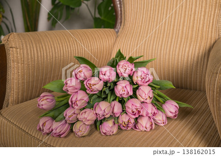 Bouquet of pink tulips on a beige armchair with greenery in the background Bouquet of pink tulips on a beige armchair with greenery in the background 138162015