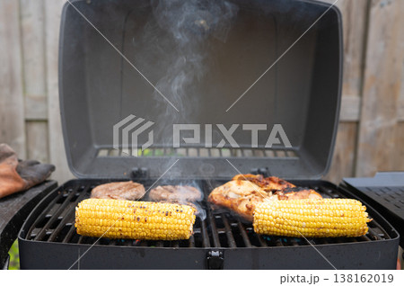 Grilling barbecue: corn and meat on outdoor gas grill in backyard setting Grilling barbecue: corn and meat on outdoor gas grill in backyard setting 138162019
