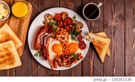 Traditional full English breakfast with fried eggs, sausages, beans, mushrooms, grilled tomatoes and bacon on wooden background. Traditional full English breakfast with fried eggs, sausages, beans, mushrooms, grilled tomatoes and bacon on wooden background. 138162136