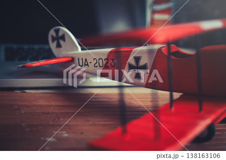 Horizontal close-up view of the tail section of a handcrafted red and white wooden triplane model, resting on a desk in a workshop. Horizontal close-up view of the tail section of a handcrafted red and white wooden triplane model, resting on a desk in a workshop. 138163106