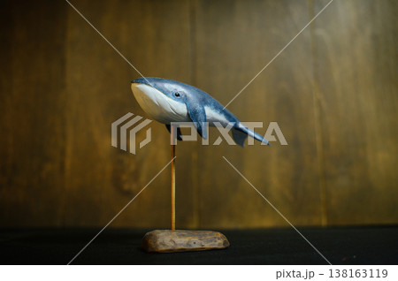 Horizontal side view of a handcrafted wooden blue whale sculpture, painted with a white underbelly and displayed on a thin metal stand with a rustic wood base. 138163119