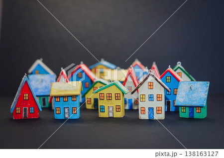 Horizontal view of a colorful collection of handcrafted miniature wooden houses, each uniquely painted with vibrant colors and snowy roofs, arranged on a dark surface. 138163127
