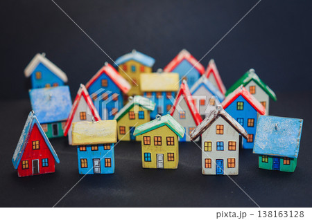 Horizontal view of a colorful collection of handcrafted miniature wooden houses, each uniquely painted with vibrant colors and snowy roofs, arranged on a dark surface. 138163128