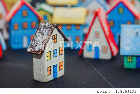 Horizontal view of a colorful collection of handcrafted miniature wooden houses, each uniquely painted with vibrant colors and snowy roofs, arranged on a dark surface. 138163133