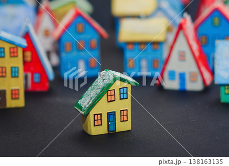 Horizontal view of a colorful collection of handcrafted miniature wooden houses, each uniquely painted with vibrant colors and snowy roofs, arranged on a dark surface. 138163135