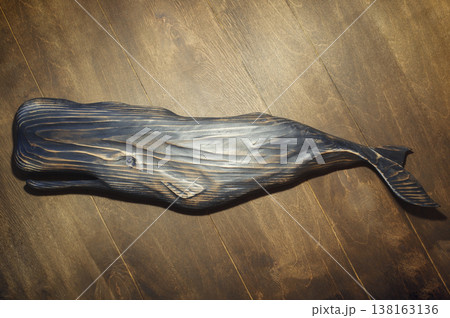Horizontal high-angle view of a large handcrafted dark wooden sperm whale sculpture with a textured, burnt finish, mounted on a wood plank wall. 138163136