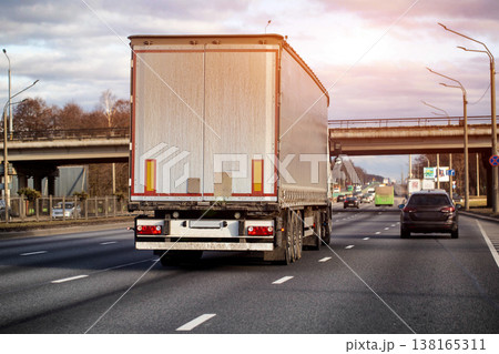 Rear view of long haul truck and trailer on multi-lane highway, transport vehicle carrying goods for logistics industry, driving on road under cloudy sky 138165311