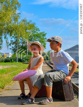 A little girl and a little boy on a train platform. A cute pair of siblings at a train station. The concept of travel, vacations, and a carefree childhood. Retro and vintage vibe. A little girl and a little boy on a train platform. A cute pair of siblings at a train station. The concept of travel, vacations, and a carefree childhood. Retro and vintage vibe. 138165467