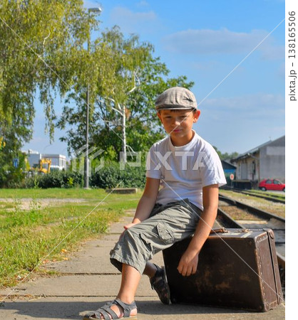 Cute boy at the train station. A little smiling boy sits on an old suitcase. The concept of travel, holiday, and carefree childhood. Retro and vintage vibe. Cute boy at the train station. A little smiling boy sits on an old suitcase. The concept of travel, holiday, and carefree childhood. Retro and vintage vibe. 138165506