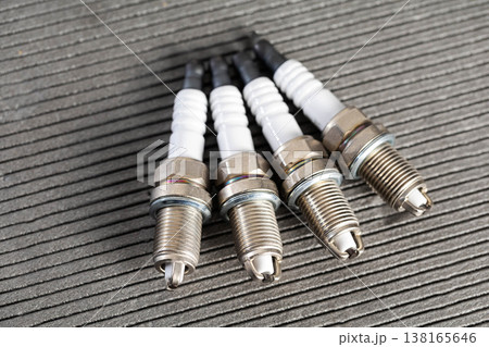 Four new vehicle engine spark plugs with white ceramic insulators and metallic bodies on dark textured surface for automotive service. Four new vehicle engine spark plugs with white ceramic insulators and metallic bodies on dark textured surface for automotive service. 138165646