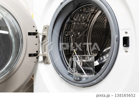 Water hardness measurement with test strip in glass cup placed inside open washing machine drum during appliance maintenance Water hardness measurement with test strip in glass cup placed inside open washing machine drum during appliance maintenance 138165652