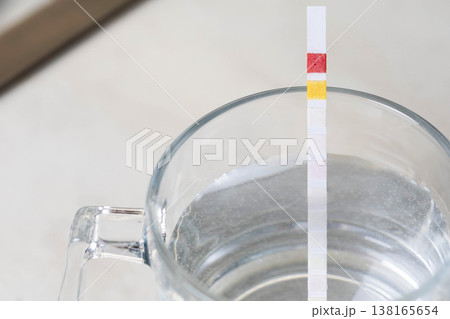 Water test strip immersion in clear glass of water displaying chemical reaction color changes measurement of water parameters for quality analysis of drinking water for safety and health purposes 138165654