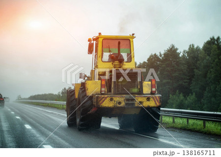 Yellow heavy construction machine moving on wet asphalt road during rain, poor visibility conditions, danger of slippery road surface. Copy space for text Yellow heavy construction machine moving on wet asphalt road during rain, poor visibility conditions, danger of slippery road surface. Copy space for text 138165711