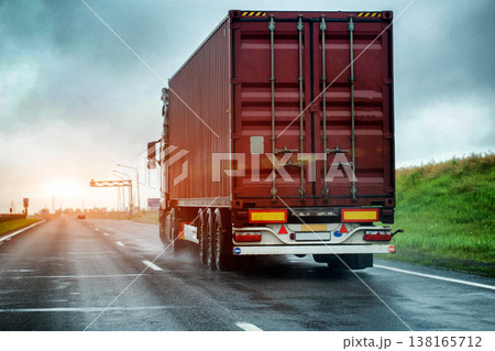 Heavy cargo truck on wet highway surface during cloudy weather conditions creating spray from tires. Transport vehicle on slippery road causing danger for drivers. Copy space for text. Container truck Heavy cargo truck on wet highway surface during cloudy weather conditions creating spray from tires. Transport vehicle on slippery road causing danger for drivers. Copy space for text. Container truck 138165712