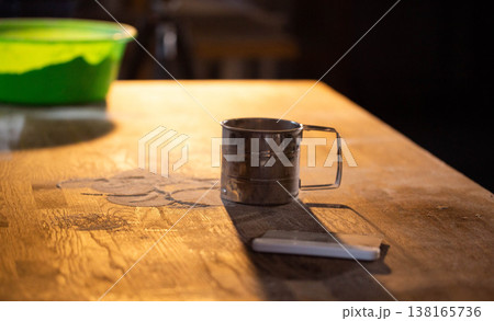 Metal flour sifter on rustic wooden kitchen table, powdery flour dust scattered. Baking preparation tool illuminated by warm light, casting long shadow. 138165736