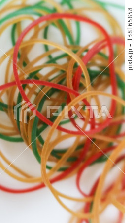 vertical photo of close up of a tangled pile of red, green, yellow and tan rubber bands on a clean white table surface with copy space 138165858