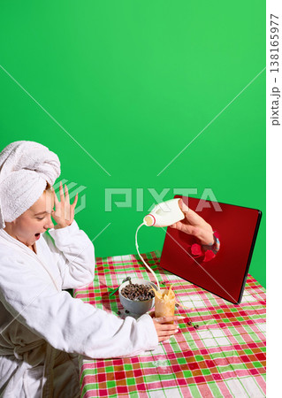 Milk pouring from tablet screen into iced coffee glass on breakfast table with woman reacting. 138165977