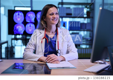 Smiling doctor reviews patient data in a modern medical office during a late afternoon consultation 138166115