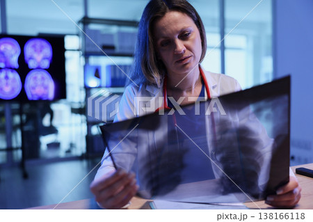 Medical professional examines chest X-ray in a modern clinic during evening hours while pondering health concerns 138166118
