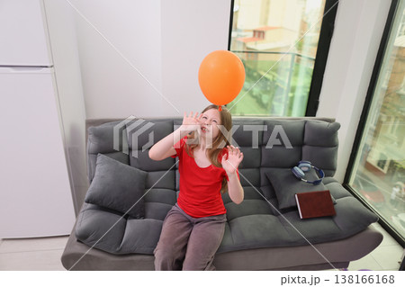 Joyful moments filled with laughter as a child plays with a bright orange balloon in a sunny living room Joyful moments filled with laughter as a child plays with a bright orange balloon in a sunny living room 138166168