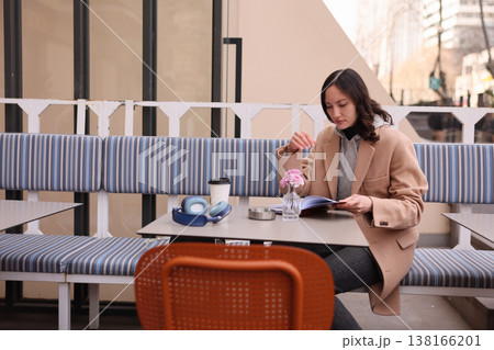 Woman enjoying a cozy moment reading a magazine while sipping coffee in a stylish outdoor cafe on a sunny day in the city 138166201