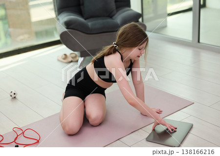 Young girl engaged in an online workout session in a modern home studio with natural light streaming through the windows 138166216